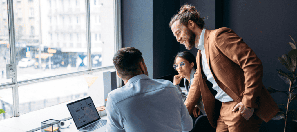 Featured image for “Fractional CAIOs Explained: The Executives That Make AI Work,” showing three professionals collaborating around a laptop in a modern office, reviewing data on the screen.